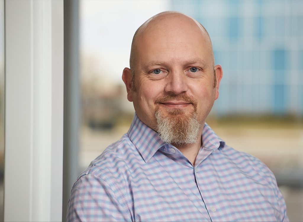 Steven Favell, in front of a window, wearing a light blue checkered shirt.